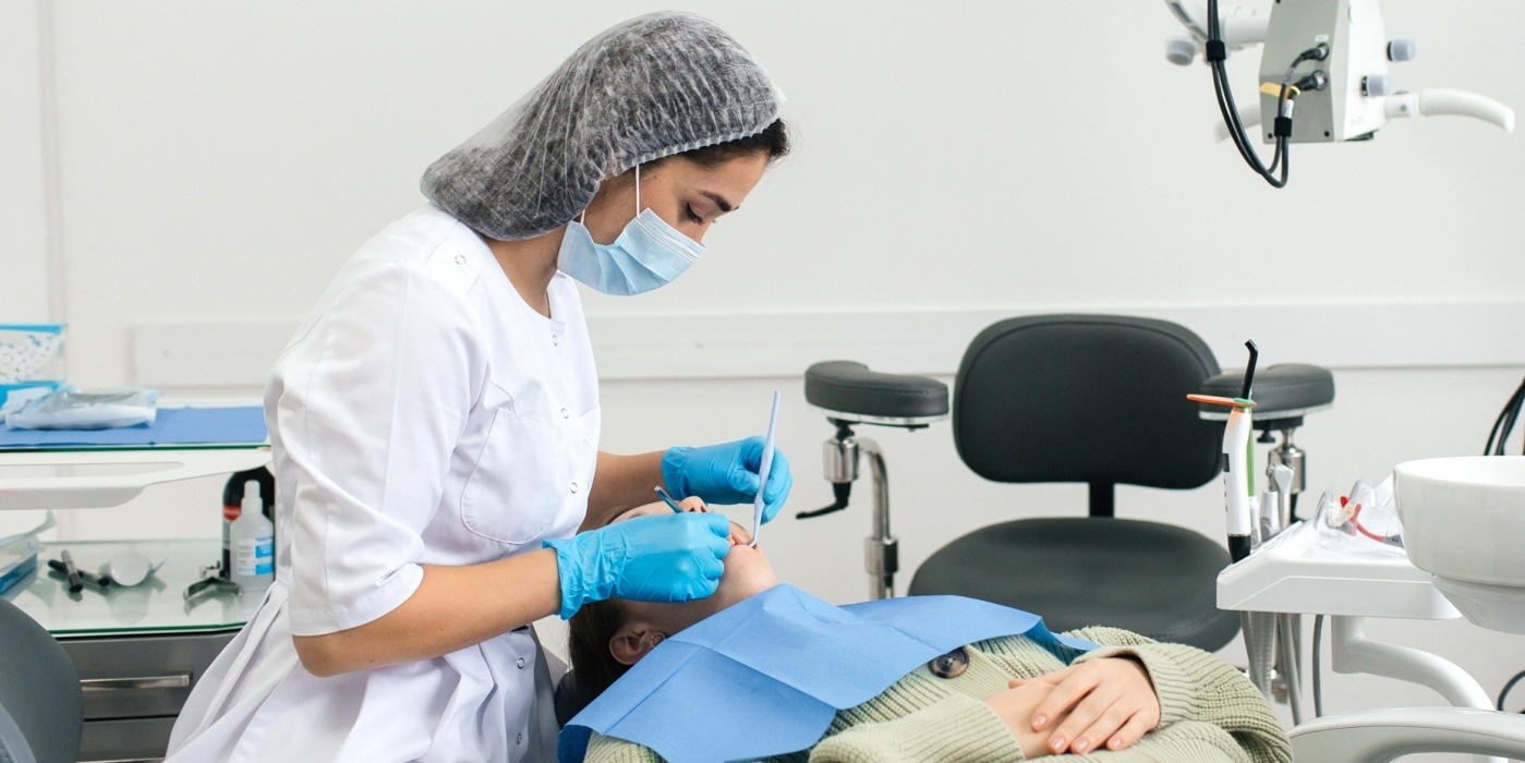 стоматолог осматривает зубы пациента перед началом лечения зубов под микроскопом