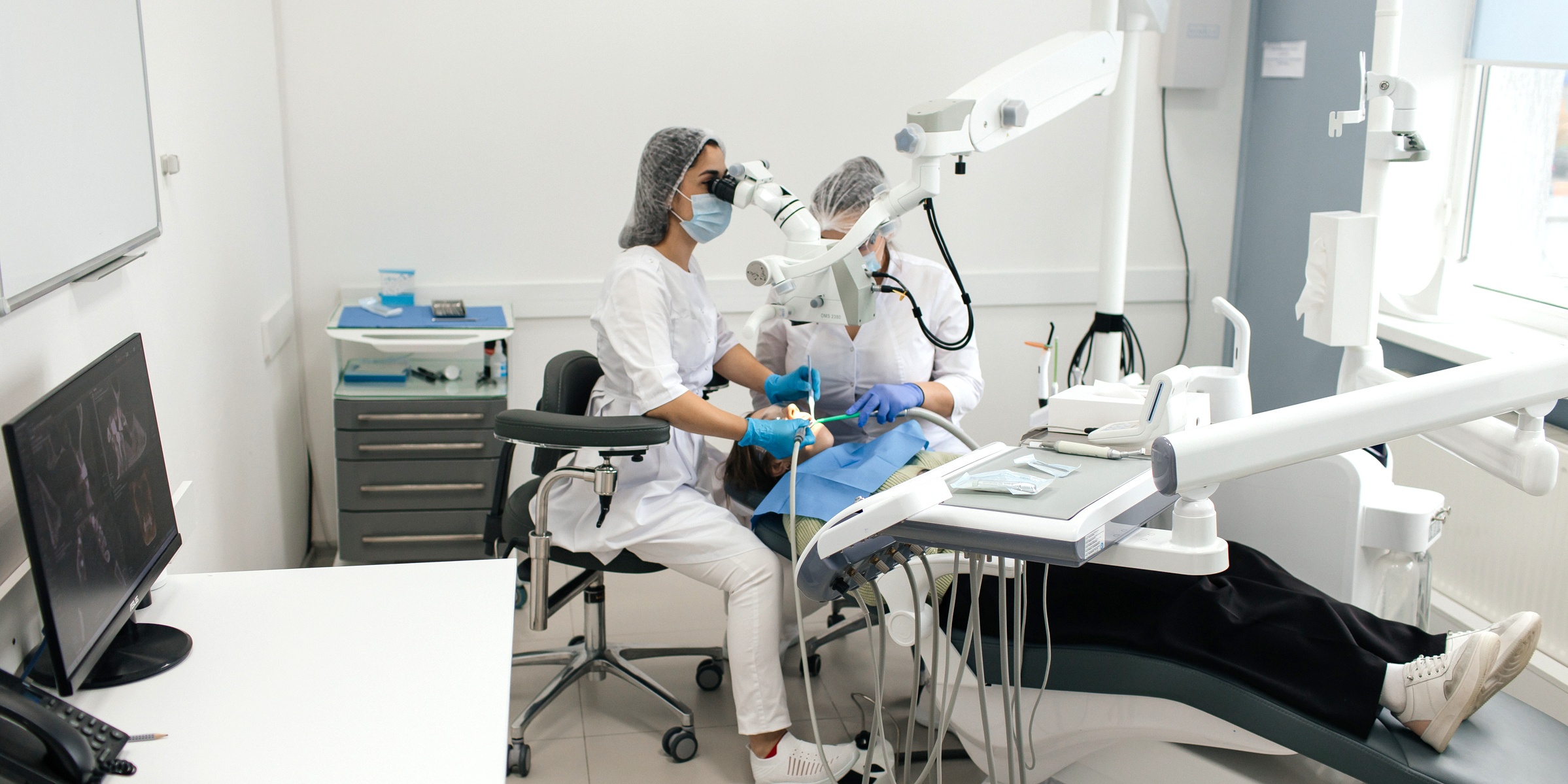 стоматолог с ассистентом проводят терапевтическое лечение зубов под микроскопом